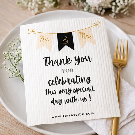White swedish cloth wedding favor with 'Mr & Mrs' design and text on a plate with gold fork and flowers.